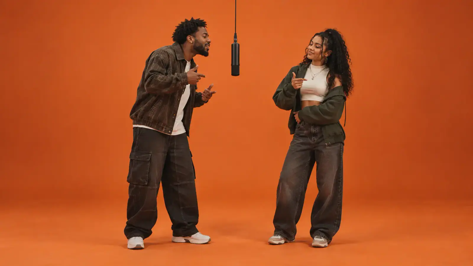 Two adult friends in a warm orange studio, positioned on opposite sides of a hanging microphone